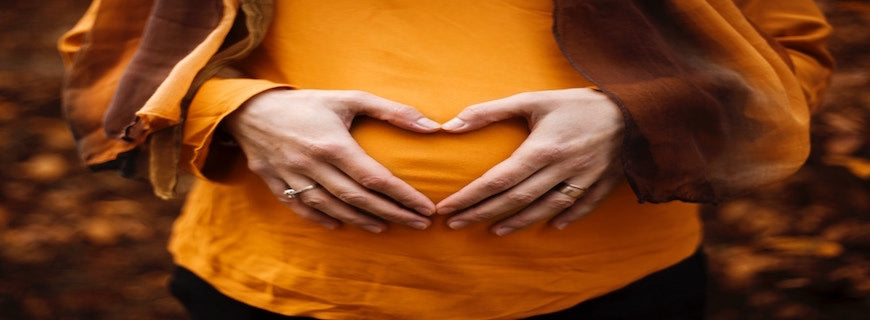 woman making love heart symbol with hands over her stomach