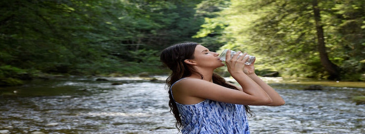 young woman drinking glass of water against river backdrop