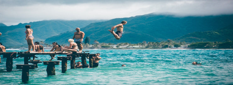 various people frolicking on jetty, with a man jumping into the ocean