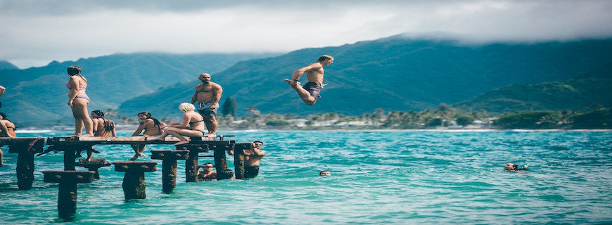 various people frolicking on jetty, with a man jumping into the ocean