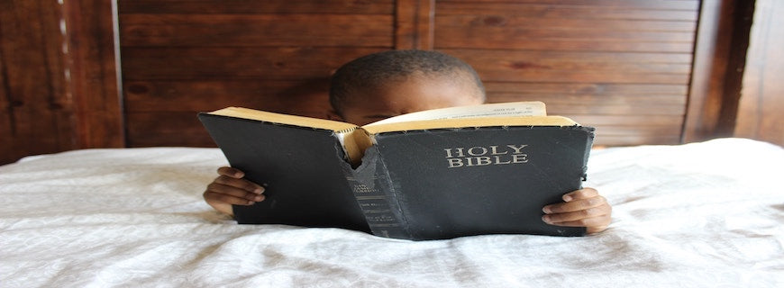 child's head appearing over the top of the Holy Bible, which he is reading