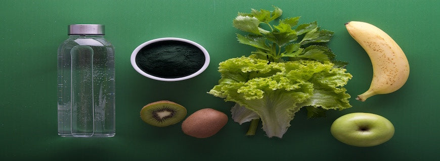 Lettuce, kiwi, apple, banana and water bottle on green backdrop