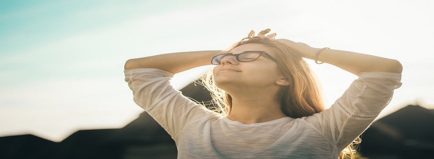 bespectacled smiling young woman with eyes closed and face bathed in sunlight