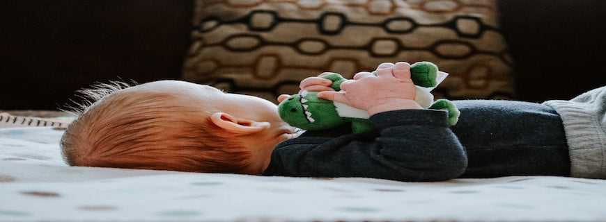 Infant laying on bed clutching soft toy dinosaur