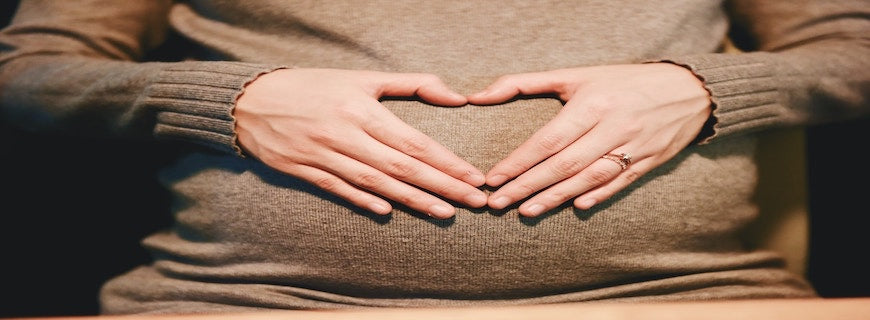 woman making love heart symbol with hands over pregnant belly