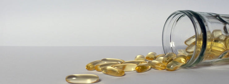 yellow pills of fish oil on a bright background with a glass jar next to it.