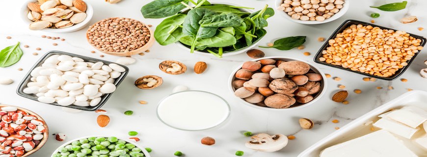 Array of vegan food, veggie protein sources: Tofu, vegan milk, beans, lentils, nuts, soy milk, spinach and seeds. Top view on white table.