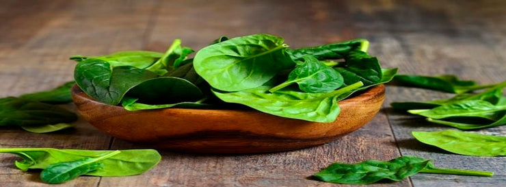 Spinach leaves in a wooden bowl on a wooden table.